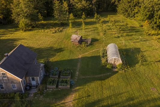 Aerial view of a well-organized one-acre homestead with house, garden, coop, and orchard at golden hour